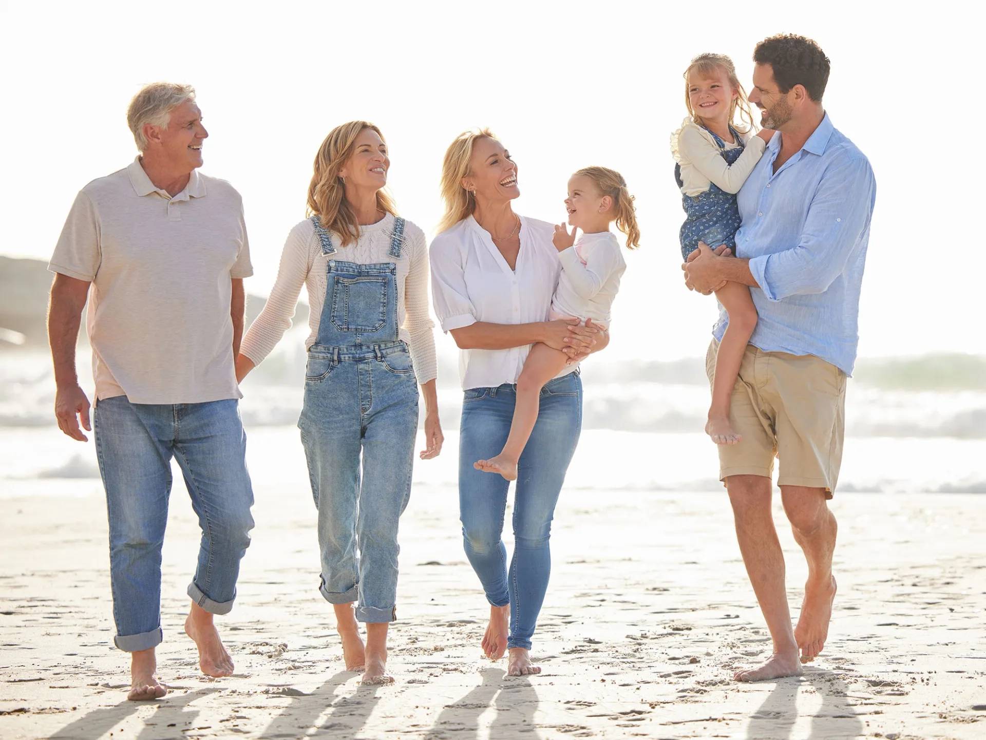 A multi-generation family walking together on a bright beach