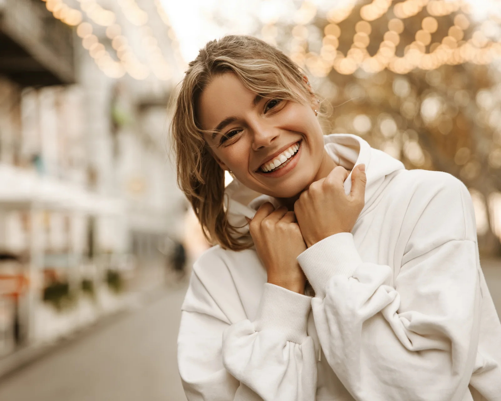 Smiling woman in a white sweatshirt on a city sidewalk